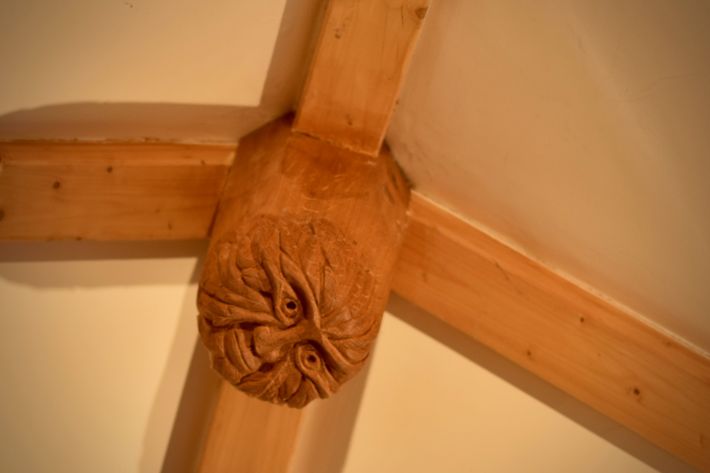 Green Man carving mounted at ceiling beam intersection